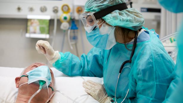 A woman helps a patient, masked. 